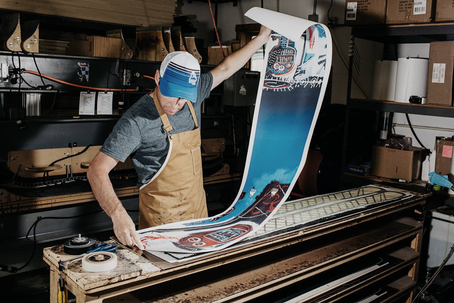 Craftsman in a workshop applies a long, colorful graphic sheet to a ski mold.
